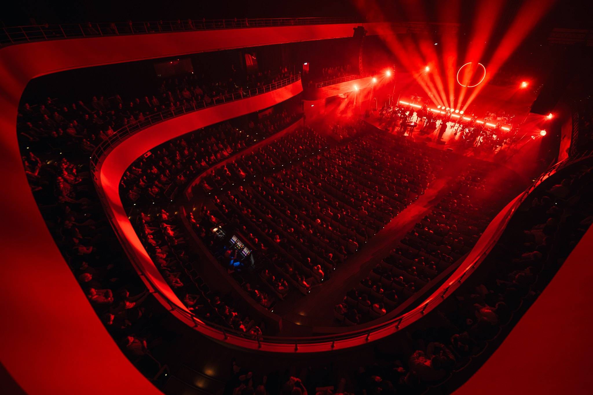 Koncert w sali z czerwonymi balkonami, światła sceniczne nad sceną
